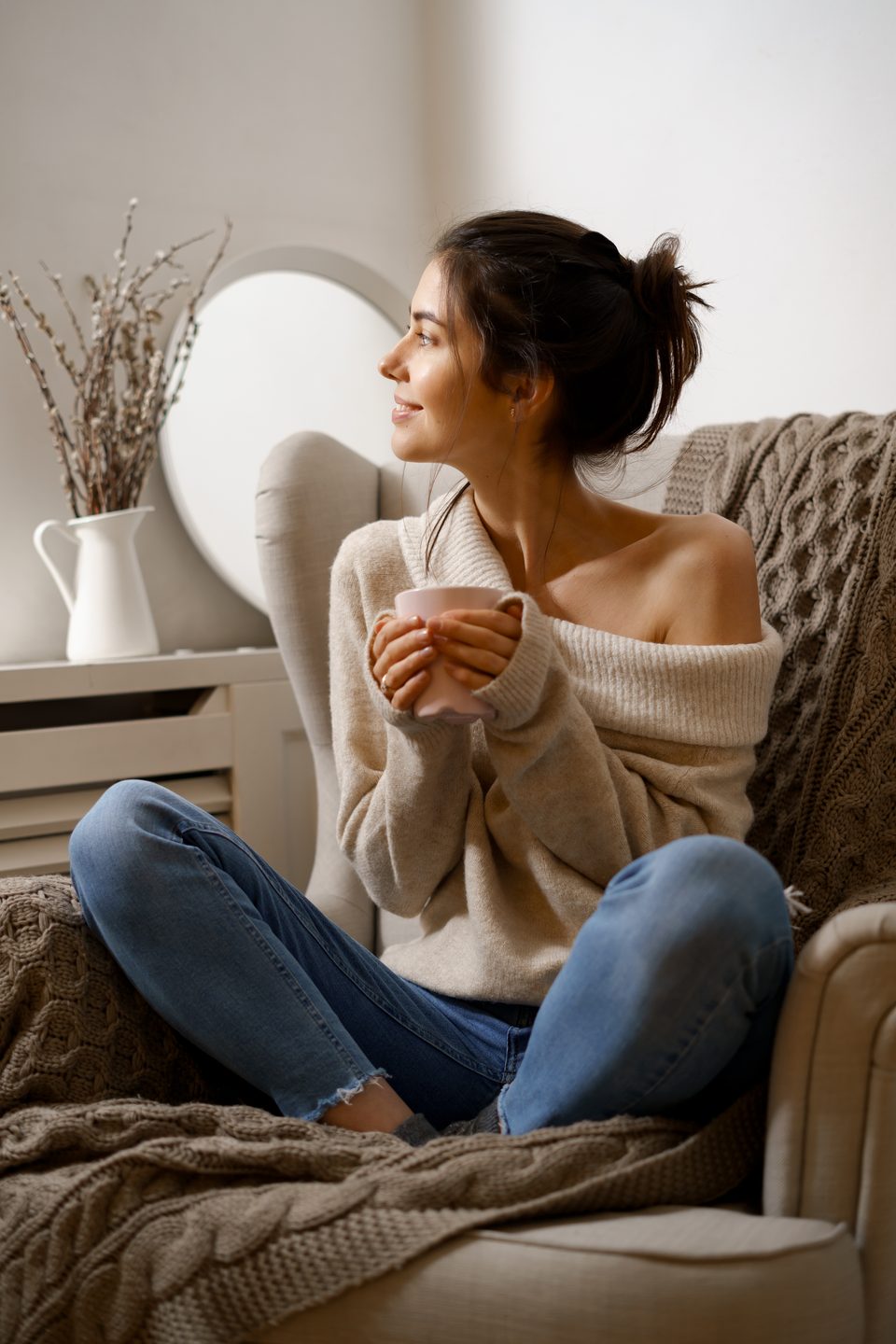 Woman with a cup of tea beside a tidy shelf and mirror in a restful room